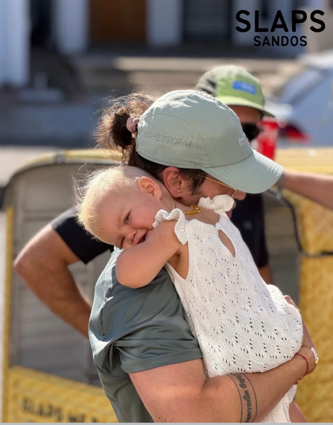 A parent carrying a baby outside the SLAPS Sandos tuk-tuk