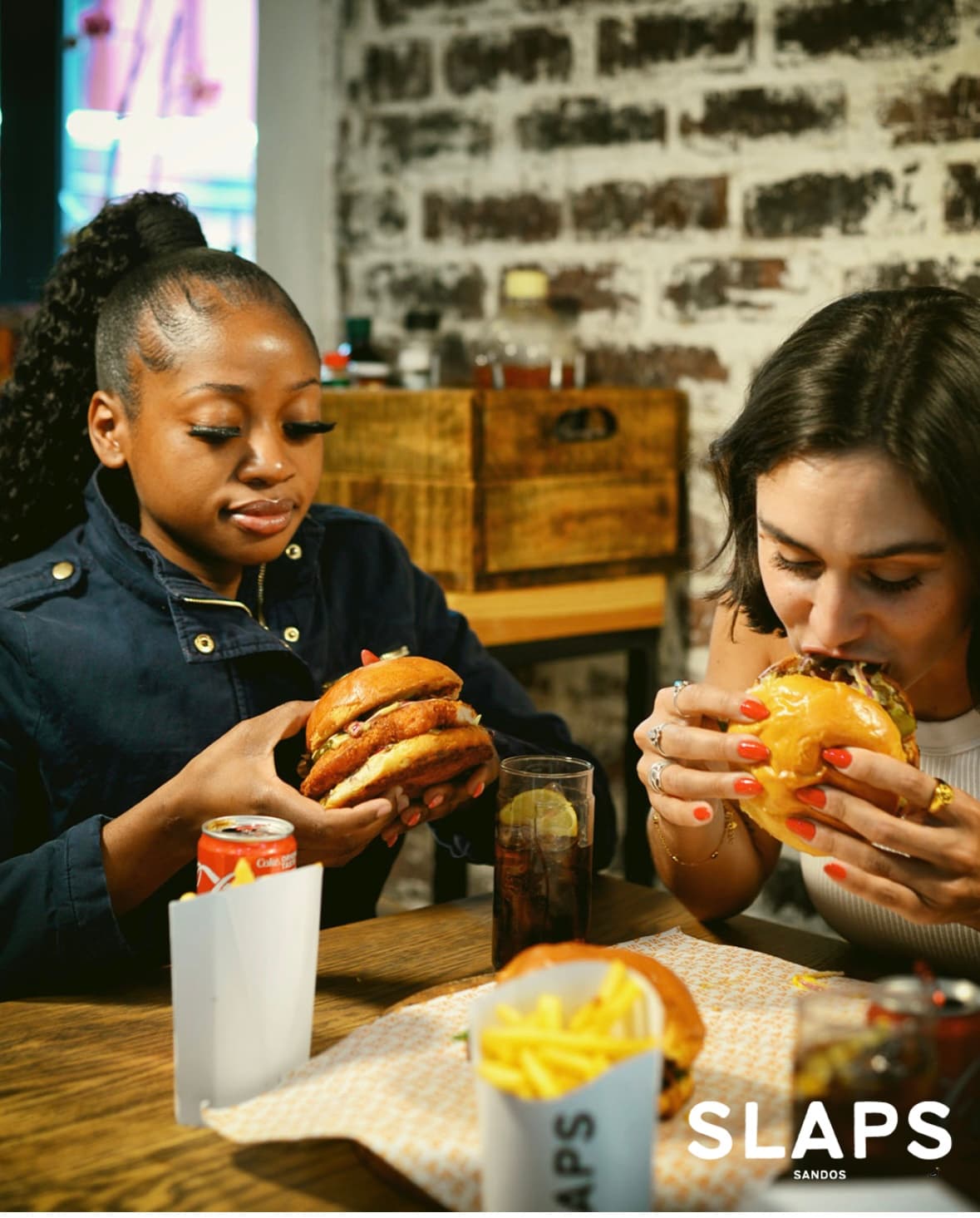 Two friends digging into SLAPS burgers at a table