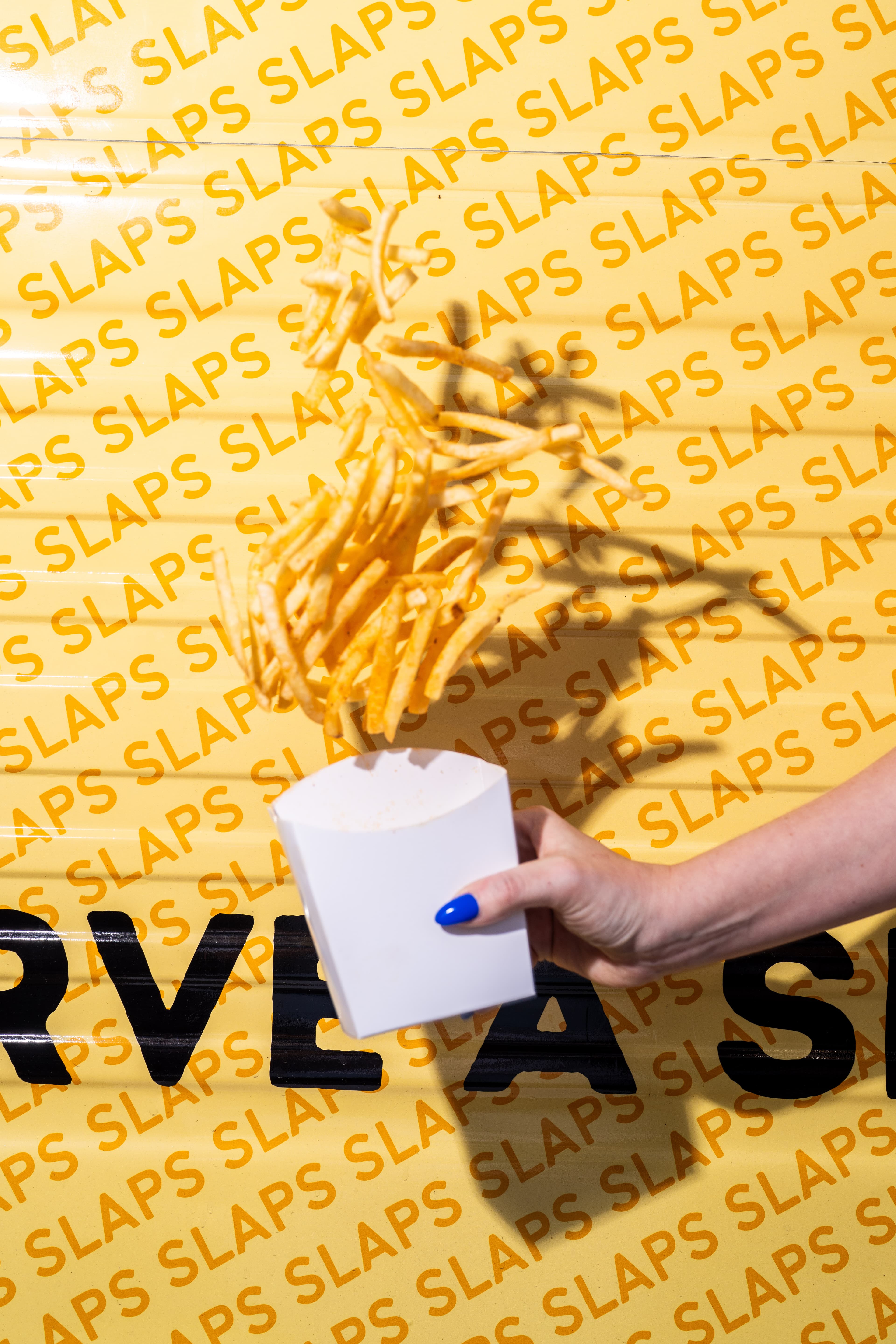 Skinny fries tossed in the air against the yellow SLAPS wrapping paper