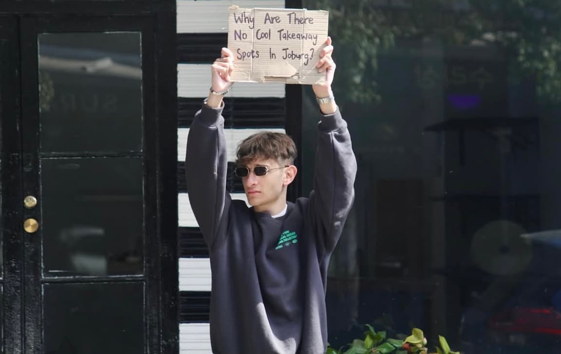 A SLAPS team member holding a handmade sign asking why there are no cool takeaway spots in Joburg